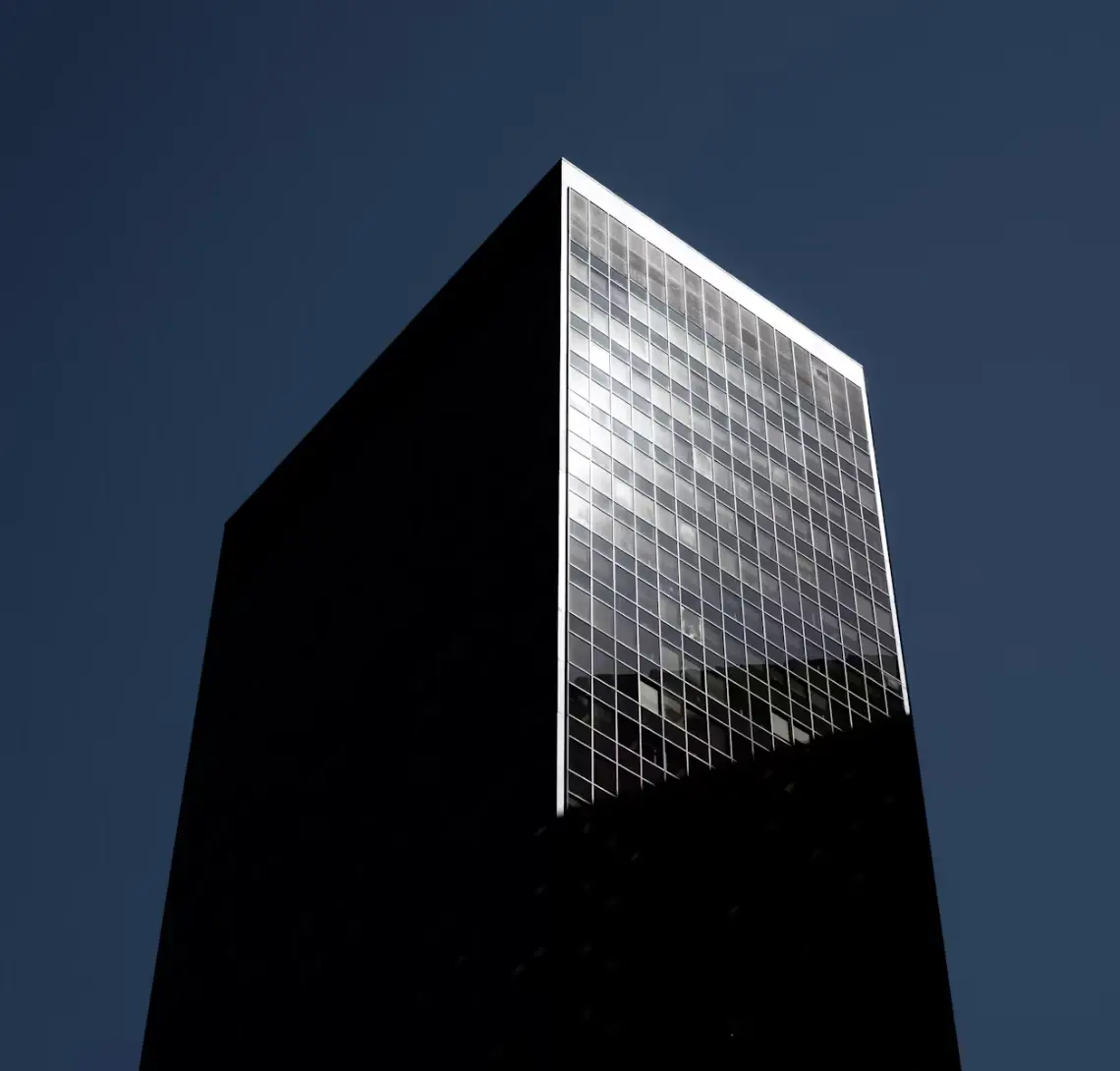 Remate de una torre a oscuras con una sola fachada de vidrio iluminada contra un cielo azul marino